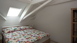 A bedroom with a sloped ceiling, a bed with floral bedding, a nightstand, and a wooden wardrobe. - Les Gîtes du Gore Virat, (Corcelles BE), by Interhome (Corcelles)