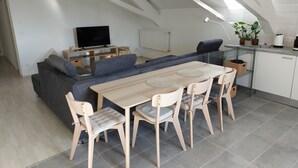 Een moderne loft met een zithoek, eethoek, bank, televisie en een keuken voorzien van planten.