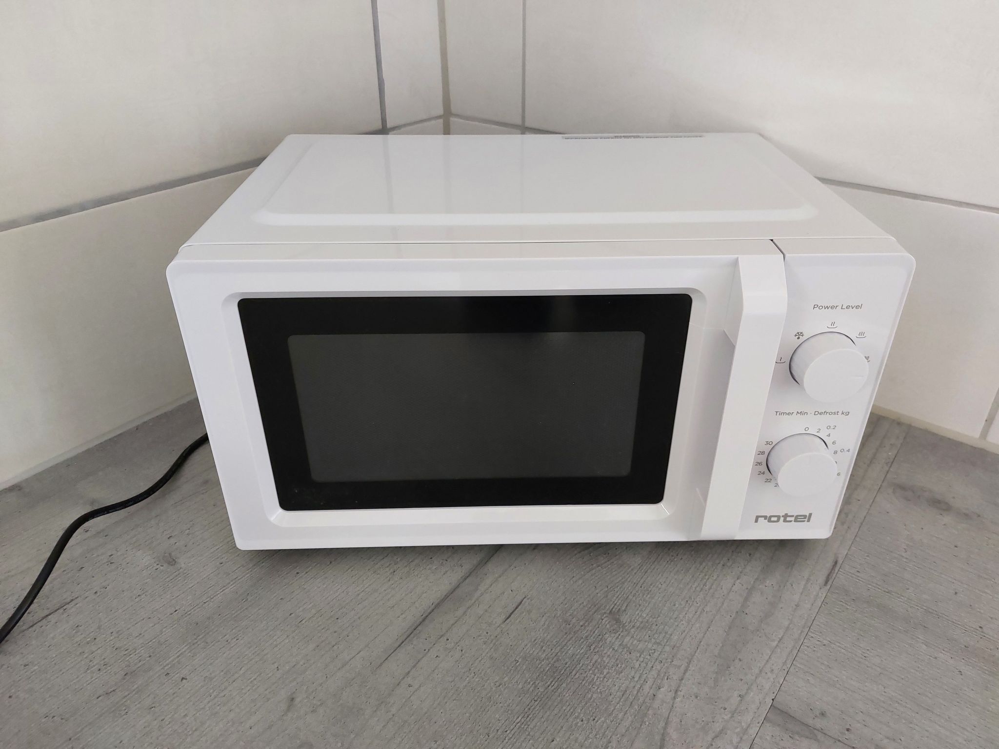 Um forno de micro-ondas branco com visor digital e botão de ajuste de potência.