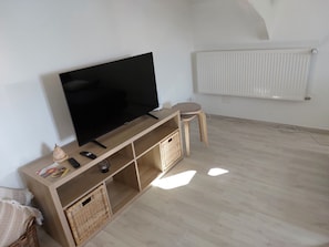 A room with a TV on a wooden stand, a radiator, and a wicker basket.
