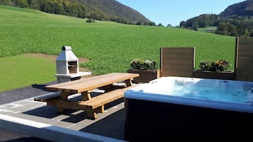 Een terras buiten met een jacuzzi, picknicktafel en barbecue.
