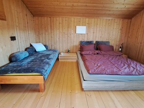 Ein Zimmer mit zwei Betten, Holzwänden, einem kleinen Tisch und einer Lampe.
