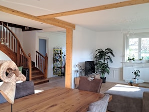 Ein geräumiges Wohnzimmer mit einer Holztreppe, einem Essbereich mit einem Holztisch und einer großen Küstertopf-Pflanze.