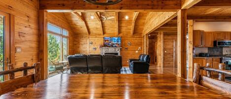 A spacious wooden interior with a large dining table, a fireplace, and a kitchen area.