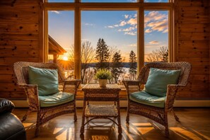 Una habitación con dos sillones de mimbre, una mesita y vistas a un paisaje boscoso al atardecer.