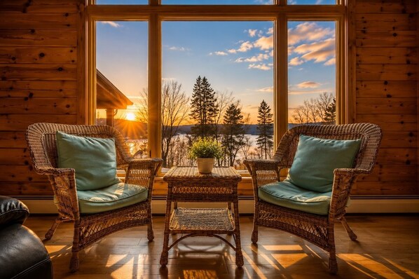 Una habitación con dos sillones de mimbre, una mesita y vistas a un paisaje boscoso al atardecer.