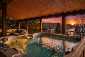Un jacuzzi con terraza de madera y vista a un atardecer sobre el agua.