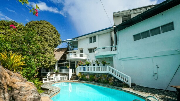 A swimming pool with a stone border, surrounded by lush greenery and a white building with a balcony. - Watson Residence w/Private pool, Billiards, and Tennis Court (Central Visayas)