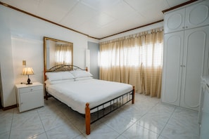 A bedroom with a bed, nightstand, lamp, mirror, wardrobe, and curtains.