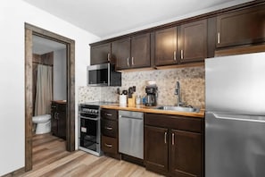 Eine kompakte Küche mit dunklen Holzschränken, einem Edelstahlkühlschrank, einer Mikrowelle und einer Kaffeemaschine.