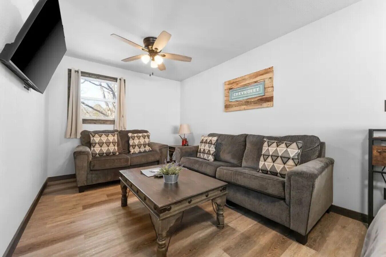 A living room with two sofas, a coffee table, a ceiling fan, a window, and a wall-mounted television.