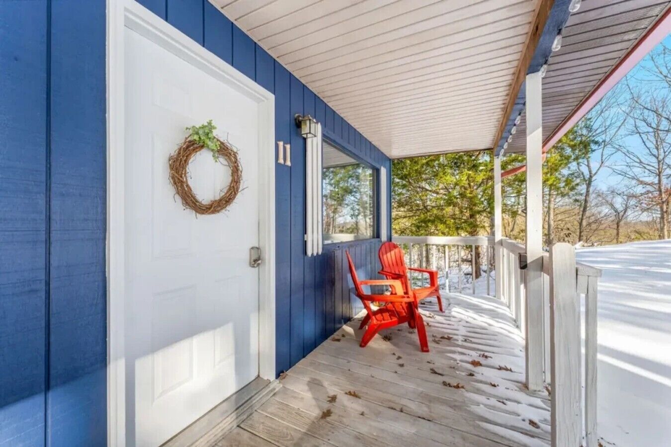 A covered porch with a white door, a red chair, and a wreath on the door.