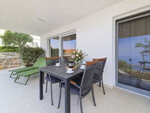 A dining area with a table set for two, chairs, a vase with flowers, and a view through a glass door. - Apartment Cvita by Interhome (Starigrad-Paklenica)