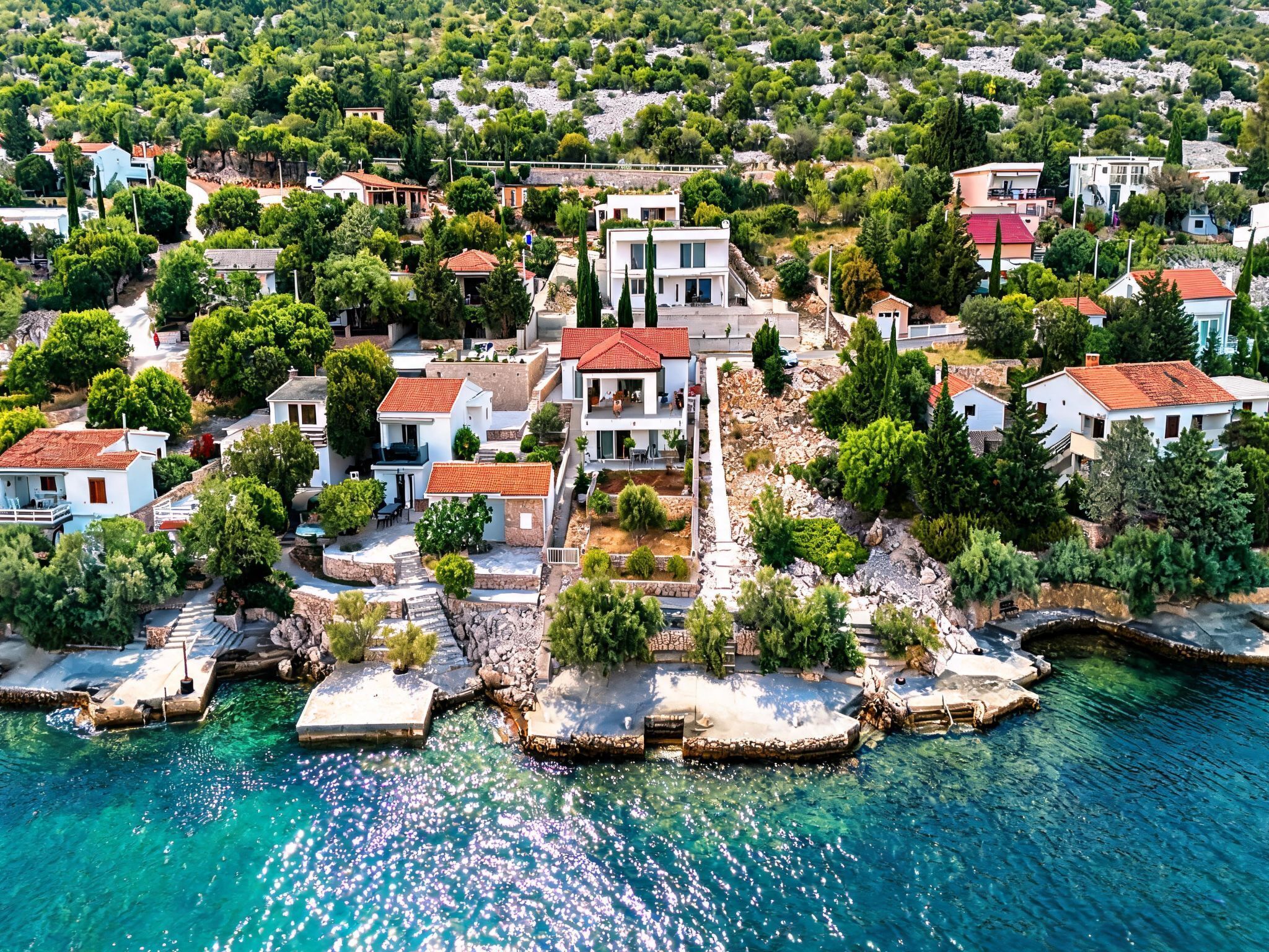 An aerial view of a coastal residential area with houses, clear blue waters, and rocky terrain.