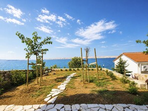 En fastighet vid kusten med en stensatt gång som leder till en pergola av trä, en stenmur och utsikt över havet.
