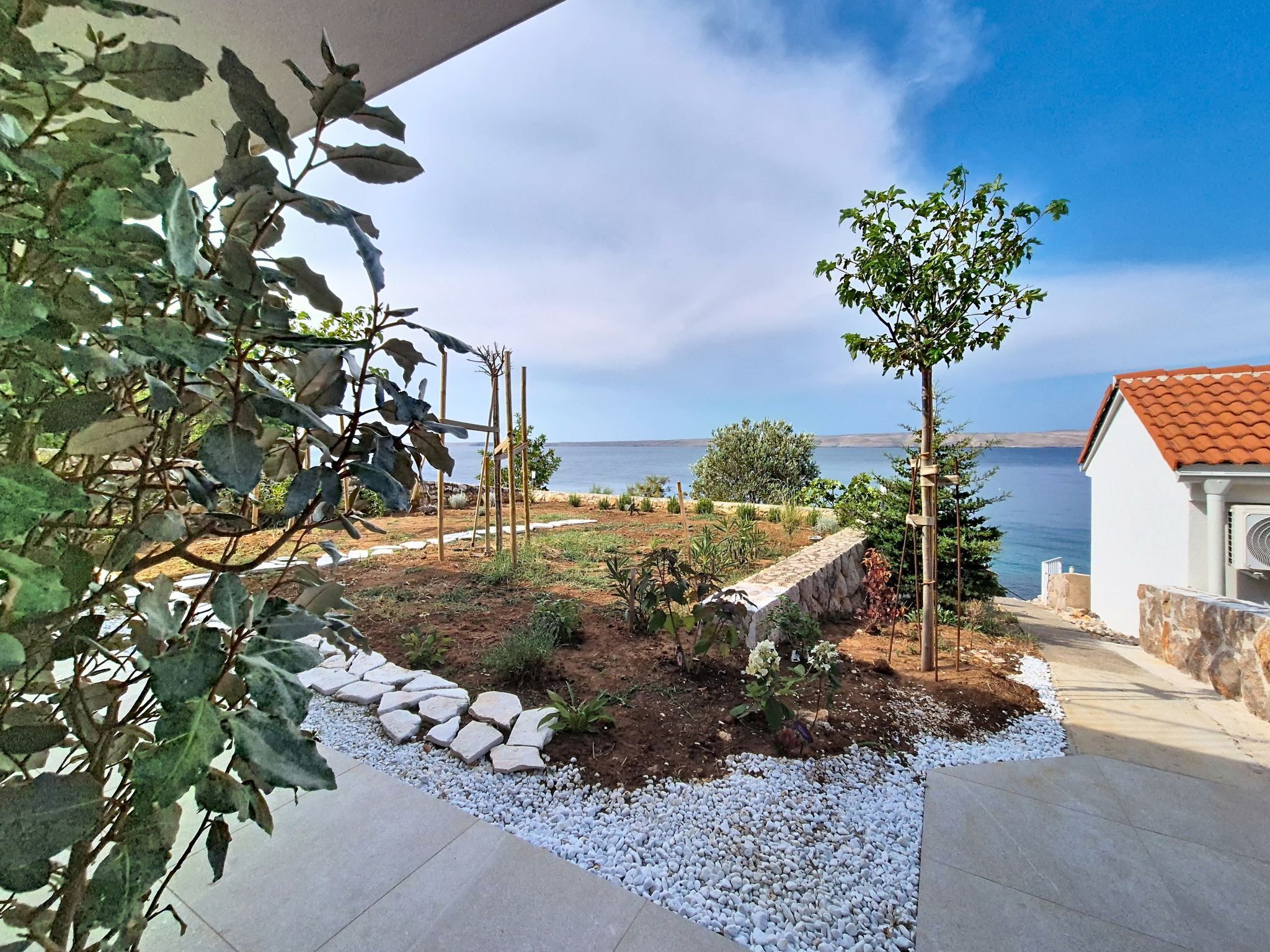 Un jardín con vistas al mar, un edificio blanco de techo rojo y un árbol.