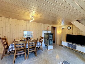 A wooden-paneled room with a dining table set for four, a television, and a clock on the wall. - Haus Wasserfall by Interhome (Saas-Almagell)