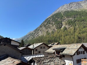 A mountain village with traditional stone-roofed buildings, a clear sky, and a forested mountain backdrop. - Haus Wasserfall by Interhome (Saas-Almagell)