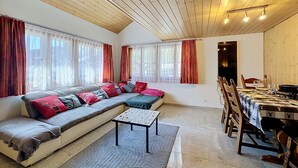 Una sala acogedora con un sofá grande, una mesa de comedor preparada para dos personas y un techo de madera.
