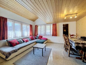 Ein gemütliches Wohnzimmer mit einer großen Couch, einem Esstisch für zwei Personen und einer Holzbalkendecke.