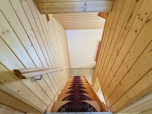 A wooden staircase with a handrail, leading to a room with a sloped ceiling. - Haus Wasserfall by Interhome (Saas-Almagell)