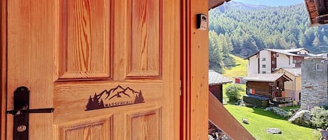 Una puerta de madera con silueta de montaña y árbol, que da a un balcón con vistas a una montaña y edificios.