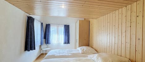 A room with two beds, a chair, and a window with curtains.