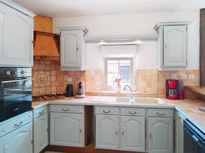 A kitchen with light blue cabinets, a stove, a sink, and a window with a view. - Maison en pierre by Interhome (Pirou)