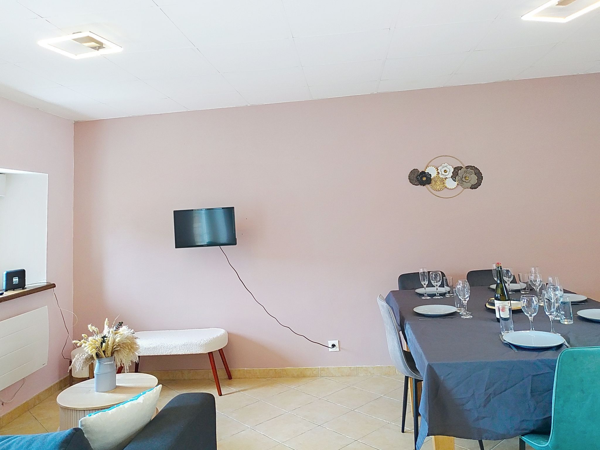 A dining area with a table set for a meal, a flat-screen TV mounted on the wall, and a decorative wall piece.
