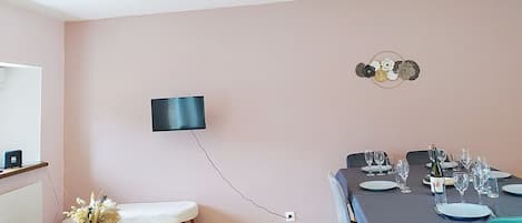 Un área de comedor con una mesa preparada para una comida, un televisor de pantalla plana montado en la pared y un adorno mural.