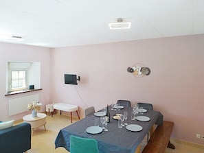A dining area with a table set for four, a flat-screen TV on the wall, and a window with a view. - Maison en pierre by Interhome (Pirou)