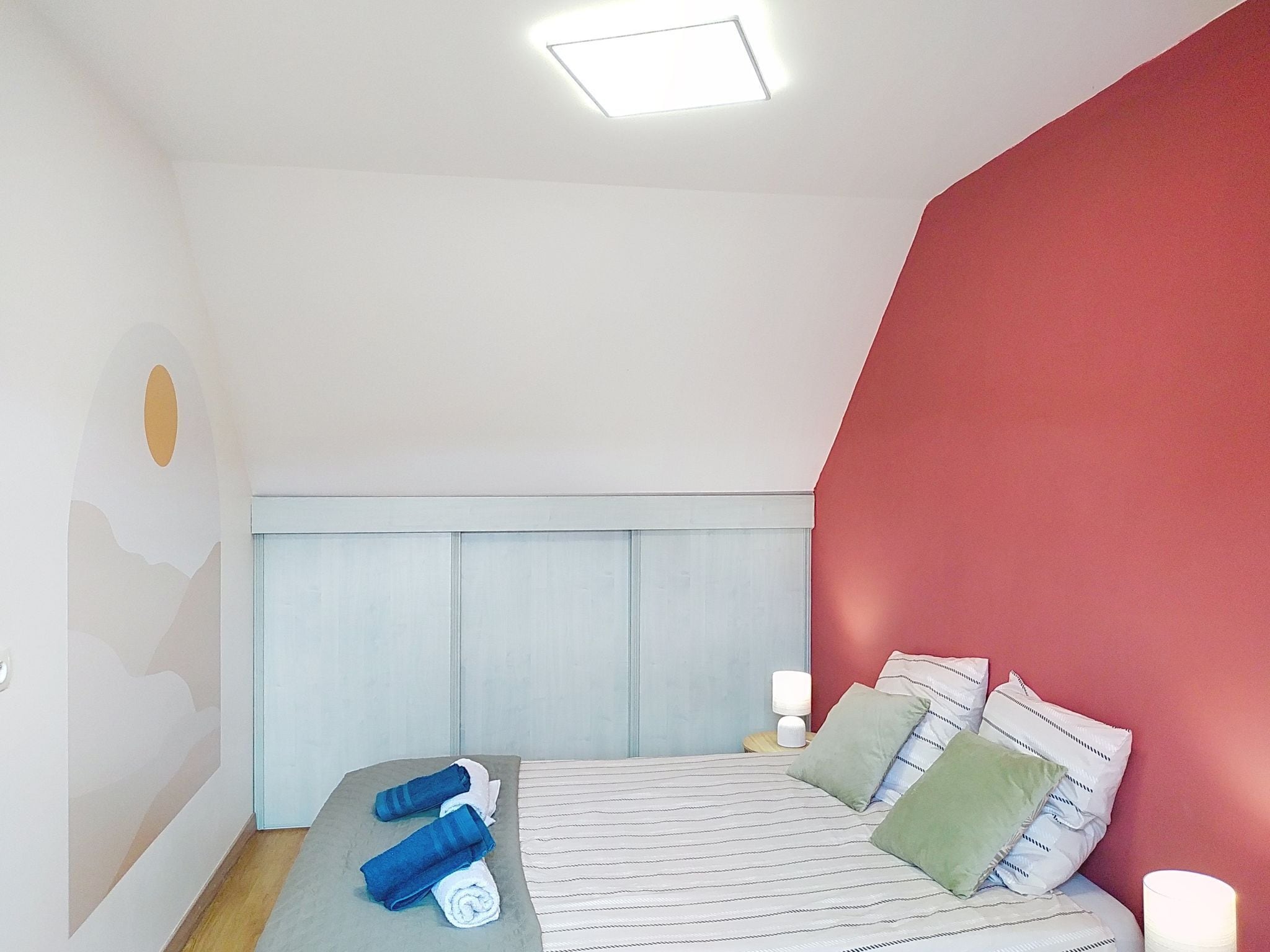A bedroom with a bed, pillows, a nightstand, and a wall with a geometric design.
