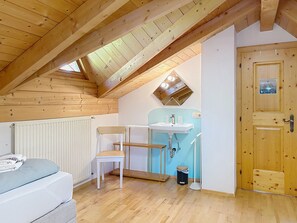 A small, cozy room with a sloped ceiling, a wooden door, a white radiator, a single bed, a chair, and a small sink. - Resimini by Interhome (Pettneu am Arlberg)