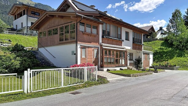 Eine zweistöckige Chalet mit geneigtem Dach, Holzfassade und weißer Außenwand.