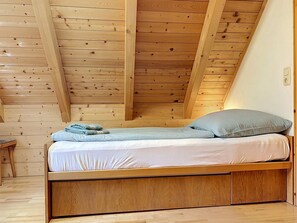 Ein Einzelbett mit Holzrahmen, einer Matratze, einem Kopfkissen und einer zusammengelegten Decke.