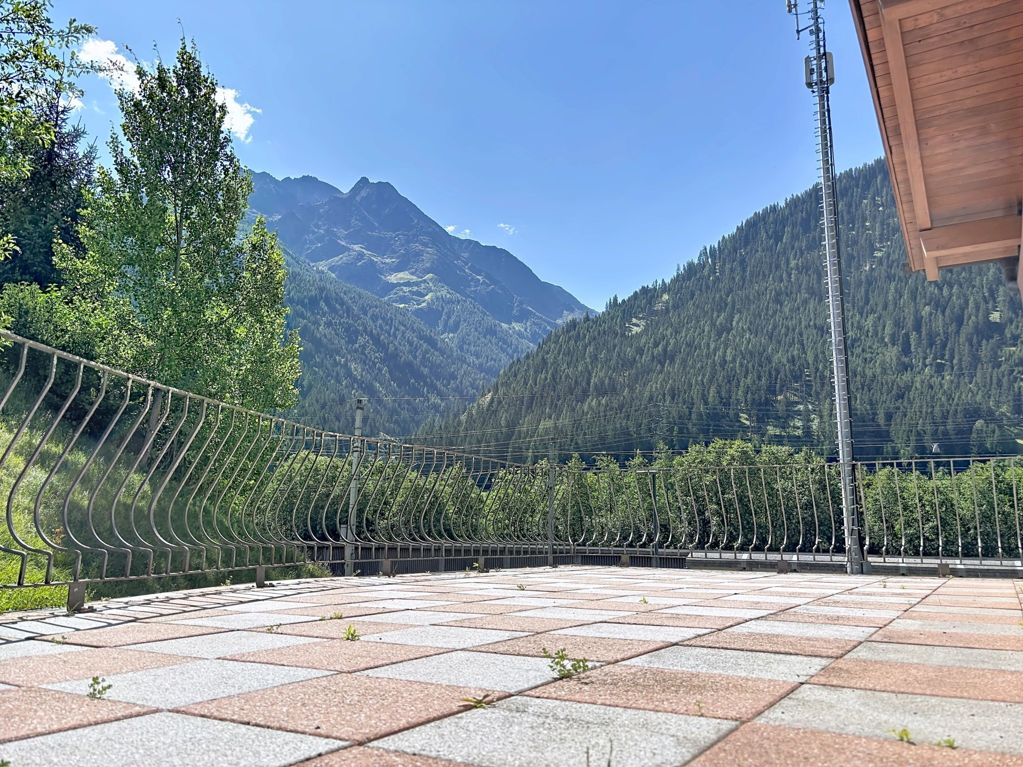 Een terras met uitzicht op bergen, een metalen hek en een houten gebouwstructuur.