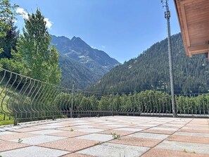 A terrace with a view of mountains, a metal fence, and a wooden building structure.