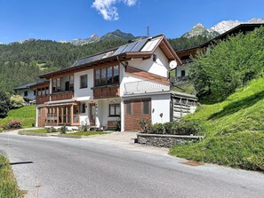 A two-story building with a balcony, a solar panel, and a mountain backdrop.