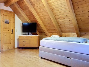 A bedroom with a wooden ceiling, a TV on a wooden cabinet, a bed with a blue pillow, and a wooden wardrobe.