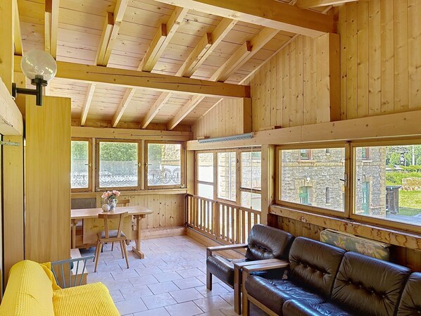 A wooden interior with a dining area, a sofa, and large windows.
