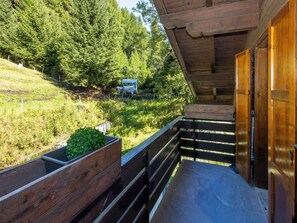 A wooden balcony with a view of a forested hillside and a small building in the distance. - Nordic Nest by Interhome (Bormio)