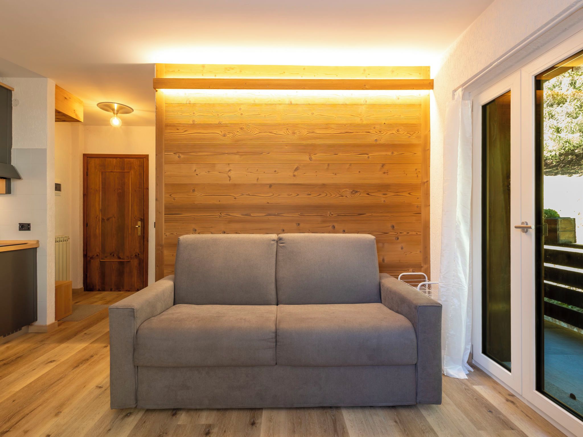Ein modernes Wohnzimmer mit einem grauen Sofa, Holzvertäfelung und einer Schiebeglasdoor zum Außenbereich.