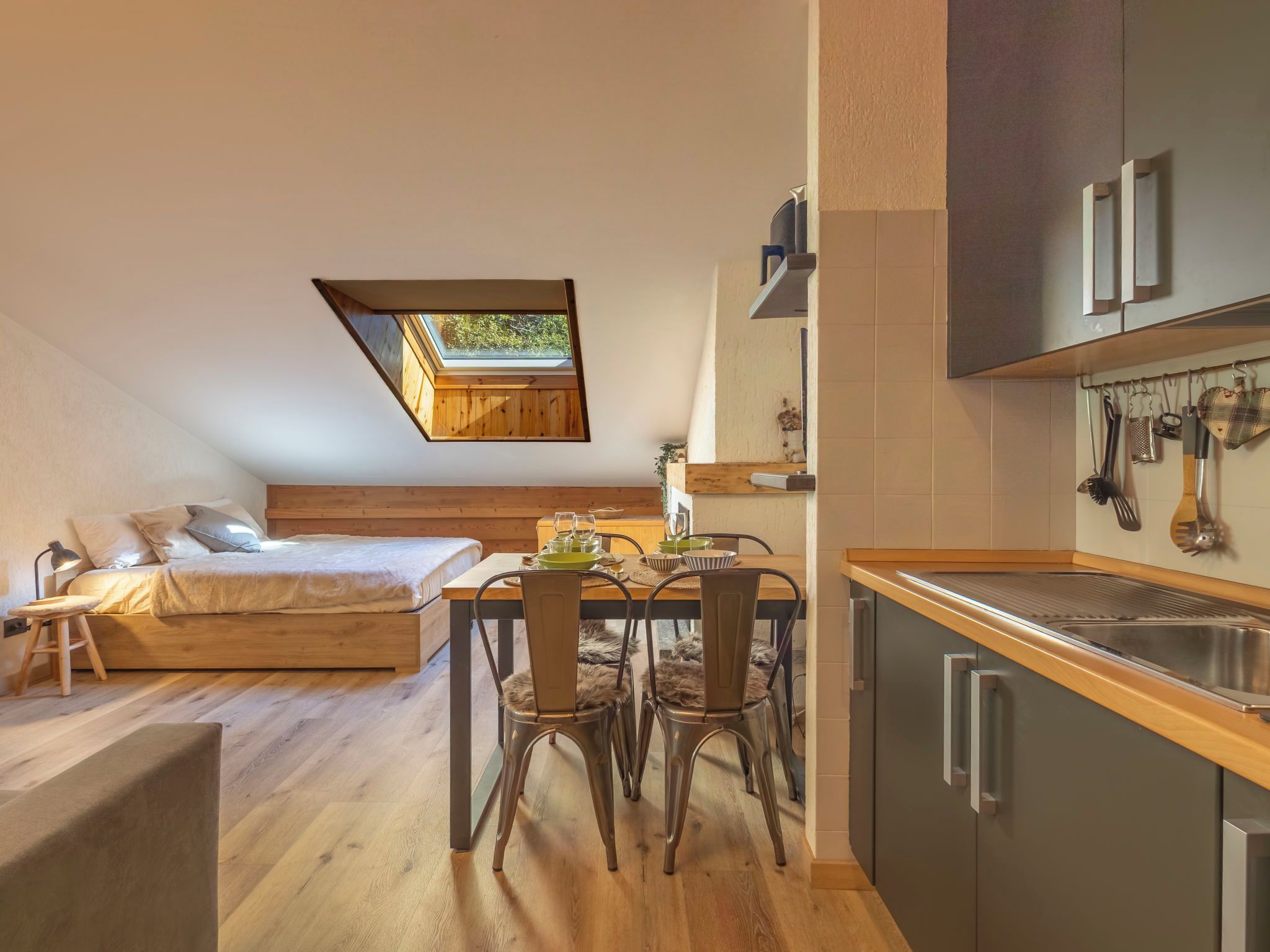 A compact bedroom with a lofted sleeping area, a dining table with chairs, and a kitchenette with hanging utensils.