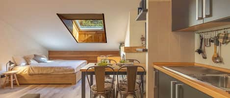 Une chambre compacte avec un espace de couchage en mezzanine, une table à manger avec des chaises et un coin cuisine équipé d’ustensiles suspendus.