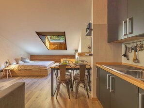 A compact bedroom with a lofted sleeping area, a dining table with chairs, and a kitchenette with hanging utensils. - Nordic Nest by Interhome (Bormio)