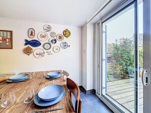 A dining area with a wooden table set for four, a glass door leading outside, and a wall decorated with various plates. - La Petite Maison du Golfe by Interhome (Le Bono)