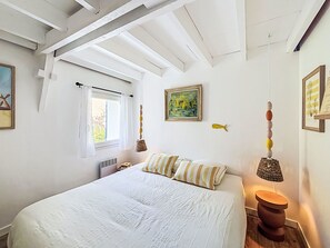 A bedroom with a large bed, a window with curtains, a radiator, a painting on the wall, and a hanging lamp. - La Petite Maison du Golfe by Interhome (Le Bono)