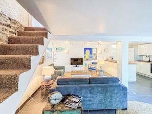 A modern living room with a sofa, coffee table, and a television. There is a staircase with a textured wall on the left. - La Petite Maison du Golfe by Interhome (Le Bono)