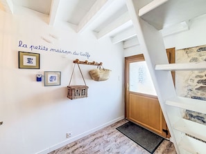 A hallway with a white wall, a wooden door, and a staircase. There are two framed pictures and a basket hanging on the wall. - La Petite Maison du Golfe by Interhome (Le Bono)