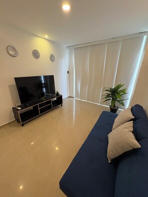 Ein modernes Wohnzimmer mit einem Flachbildfernseher, einem dunkelblauen Sofa und einem Blumentopf.